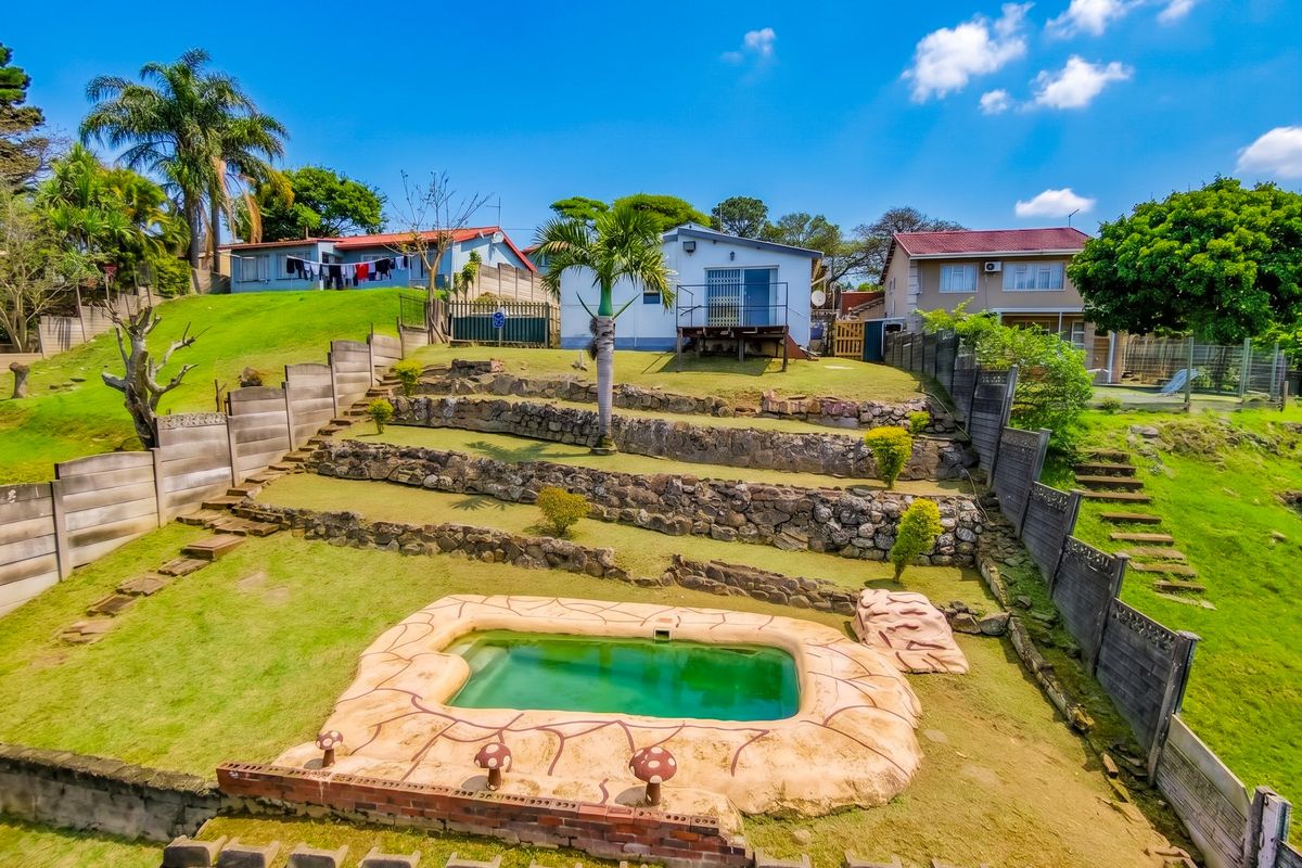 Rear view of the property featuring a terraced garden with stone retaining walls, a swimming pool, and a raised timber deck leading to the house.