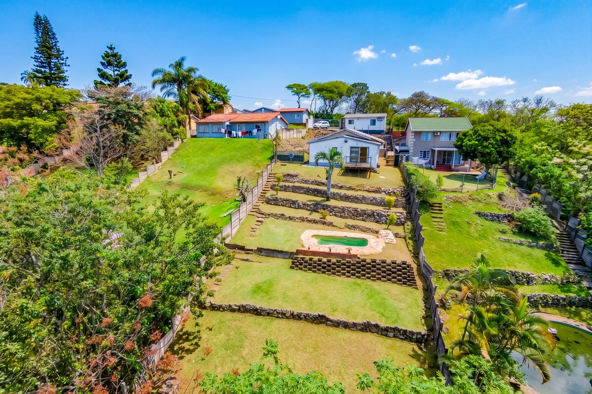 Aerial view of a residential property featuring a terraced garden, swimming pool, and multiple dwellings set on a sloped landscape.