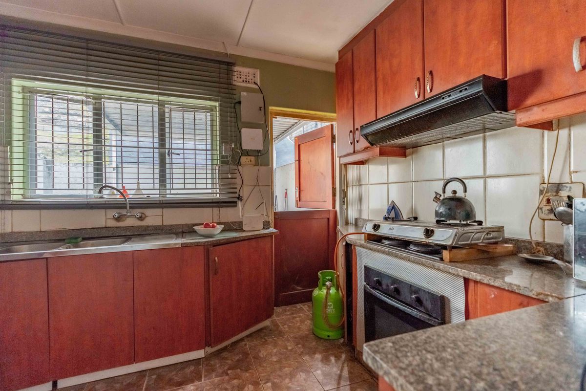 A functional kitchen featuring laminate cabinetry, granite countertops, a built-in oven with extractor fan, and tiled finishes throughout.