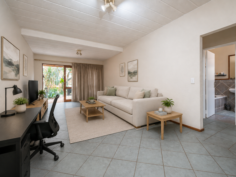 A bright living room featuring tiled flooring, exposed beam ceilings, and a sliding glass door providing access to the outdoor area.