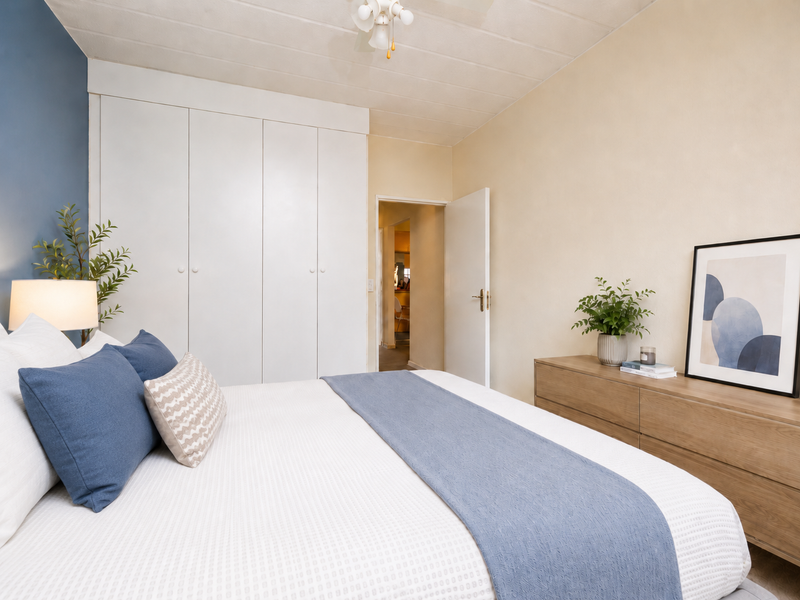 A well-maintained bedroom featuring a large built-in wardrobe, neutral wall finishes, and a ceiling fan, offering a comfortable and functional living space.