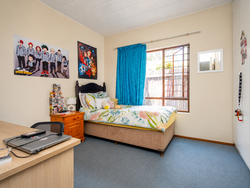 A functional bedroom featuring carpet flooring, a built-in wardrobe, and a window fitted with security bars for added safety.