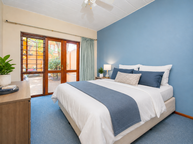 A well-lit bedroom featuring blue accent walls, carpeted flooring, and direct access to an outdoor patio area through timber-framed glass doors.