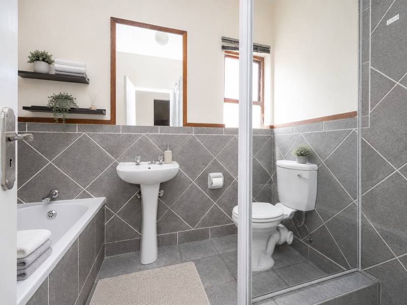 A well-maintained bathroom featuring a pedestal basin, toilet, bathtub, and a separate shower enclosure with grey diamond-patterned wall tiling.