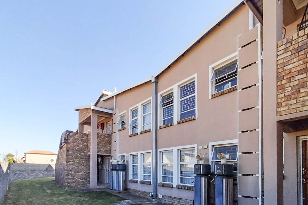 Rear exterior view of the townhouse complex featuring a brick and plaster facade, external geysers, and a shared lawn area.