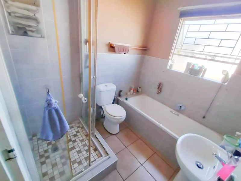 A functional bathroom featuring a separate shower enclosure, bathtub, toilet, and washbasin with tiled flooring and natural light from a window with security bars.