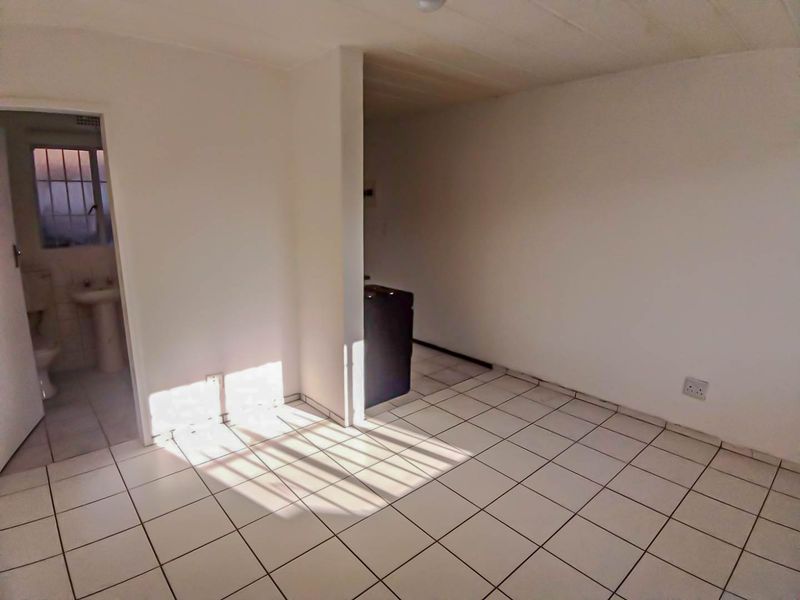 An empty, tiled living area with neutral walls and direct access to an adjacent bathroom, offering a blank canvas for renovation.