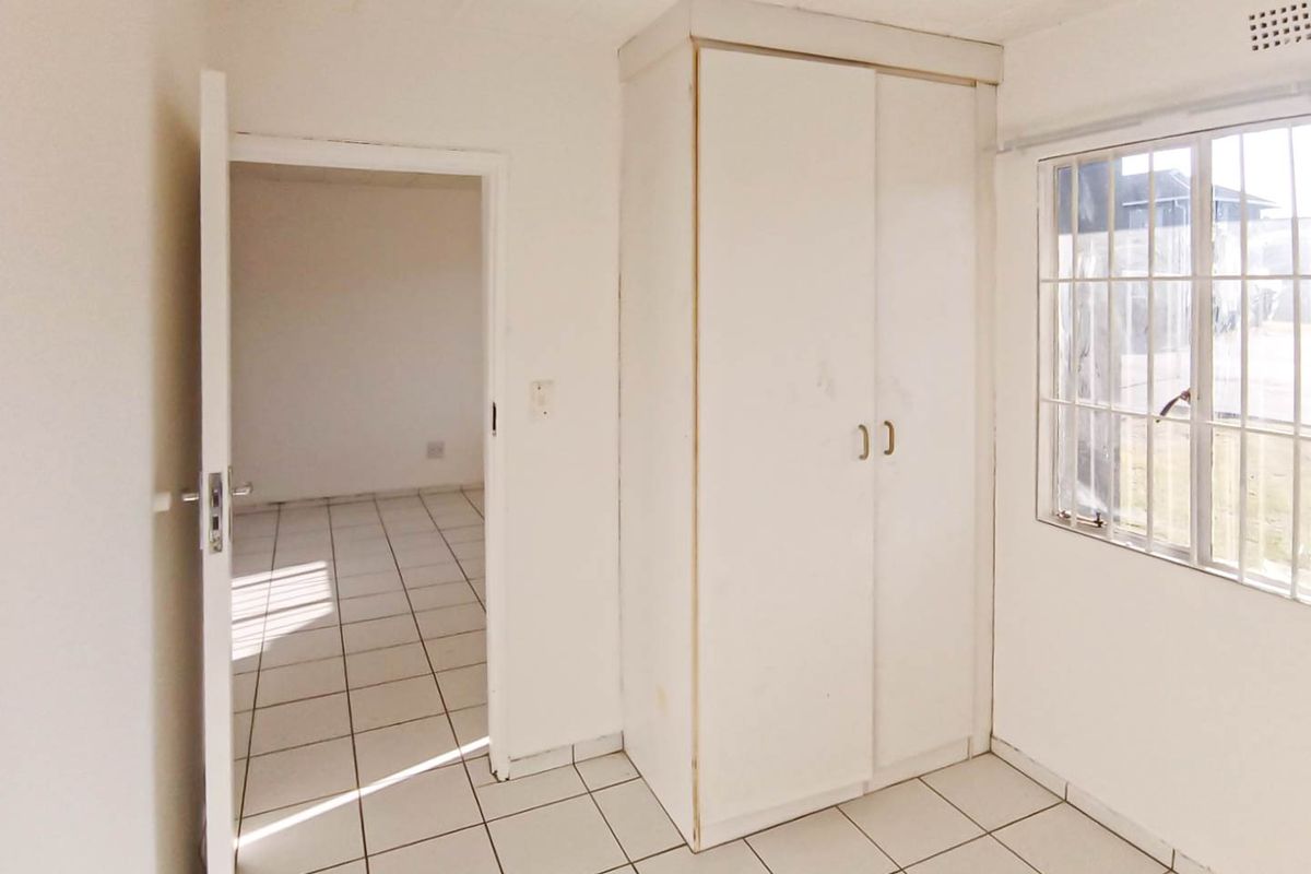 An empty bedroom featuring tiled flooring, a built-in wardrobe, and a window with security bars, offering a blank canvas for renovation.