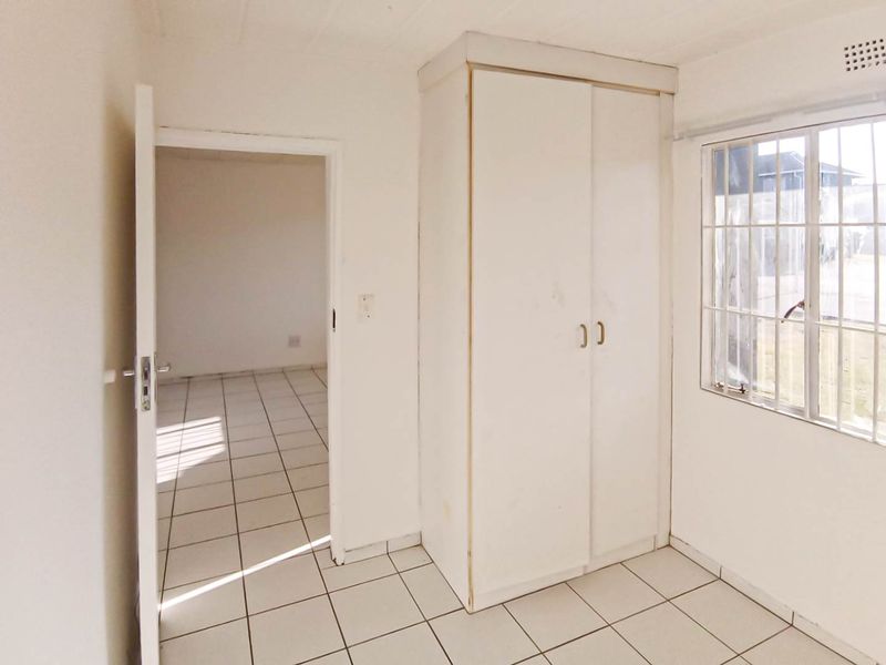 An empty bedroom featuring tiled flooring, a built-in wardrobe, and a window with security bars, offering a blank canvas for renovation.