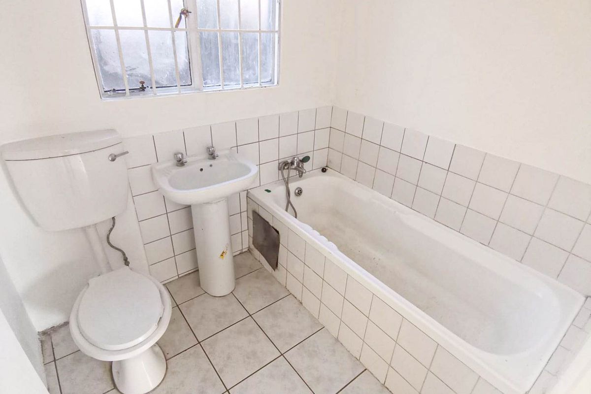A functional bathroom featuring a pedestal basin, toilet, and bathtub with tiled splashbacks and flooring, requiring cosmetic updates to modernize the space.