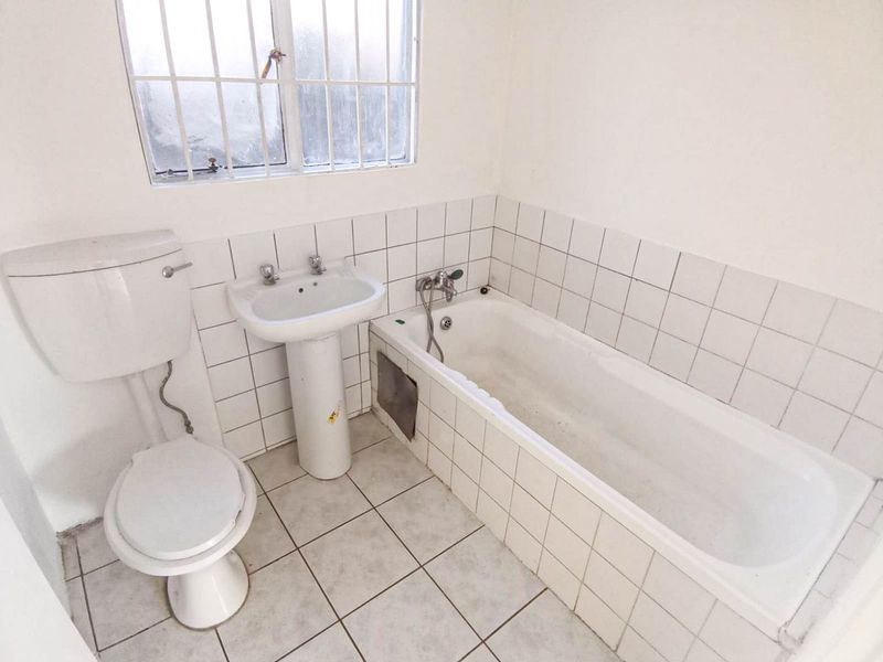 A functional bathroom featuring a pedestal basin, toilet, and bathtub with tiled splashbacks and flooring, requiring cosmetic updates to modernize the space.