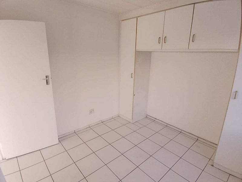 A vacant bedroom featuring white tiled flooring and built-in storage cupboards, offering a clean and neutral space ready for personalization.