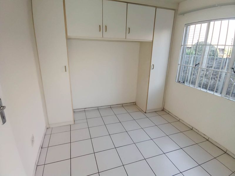 A vacant bedroom featuring white built-in cupboards, tiled flooring, and a window fitted with security bars.