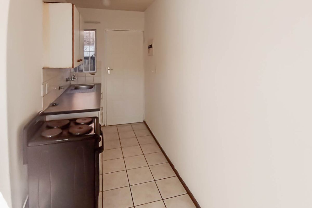 A compact kitchen featuring tiled flooring, built-in cabinetry, a stainless steel sink, and a freestanding stove, offering a functional layout for renovation.
