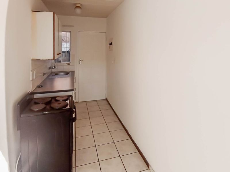 A compact kitchen featuring tiled flooring, built-in cabinetry, a stainless steel sink, and a freestanding stove, offering a functional layout for renovation.