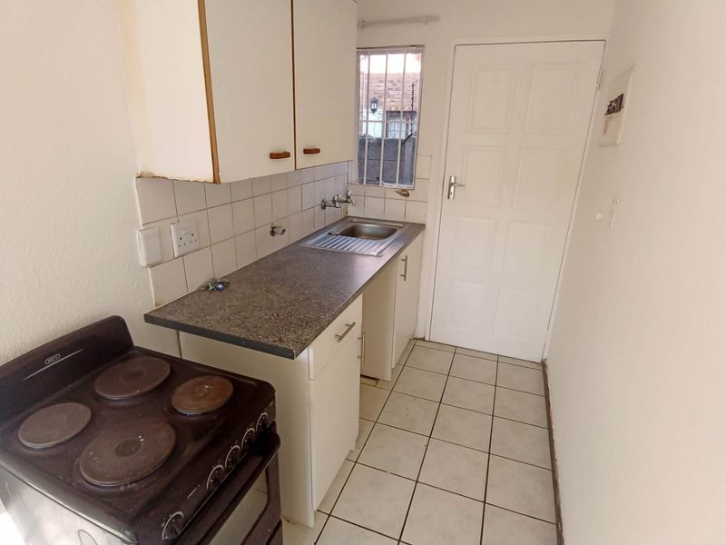 A compact kitchen featuring built-in cabinetry, a stainless steel sink, tiled backsplash, and ceramic flooring, offering a functional space ready for modernization.
