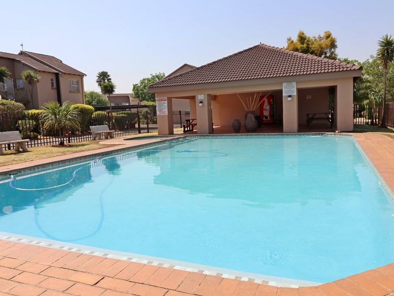 A well-maintained communal swimming pool area featuring brick paving and a covered patio structure within a townhouse complex.