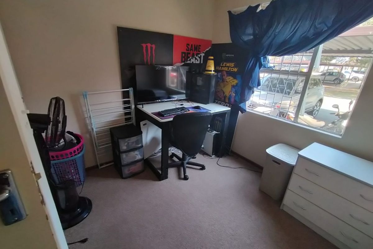 A standard bedroom featuring carpeted flooring and a window with security bars, currently utilized as a home office space.