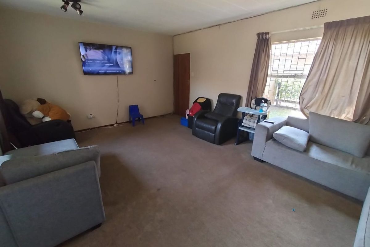 A spacious living room featuring carpeted flooring, security bars on the window, and a ceiling-mounted spotlight fixture.