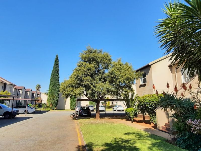 A view of the townhouse complex exterior featuring paved driveways, covered carports, and well-maintained communal garden areas under a clear blue sky.