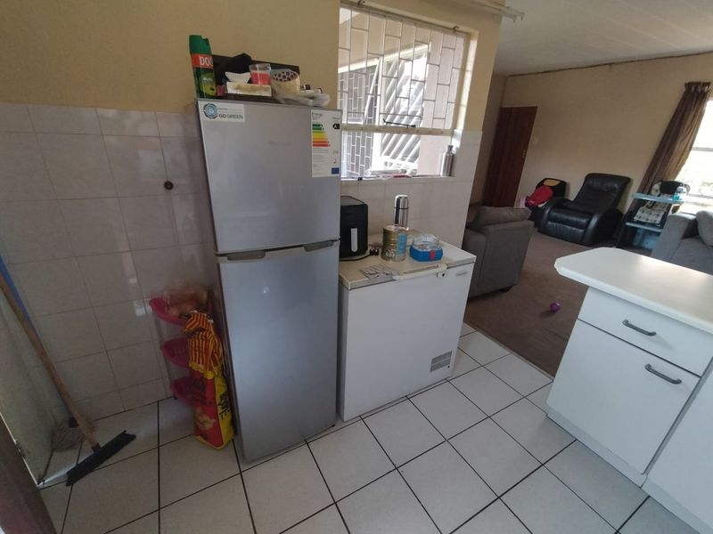 Open plan kitchen and living area featuring tiled flooring, security window bars, and basic cabinetry, offering a functional layout with potential for modernization.