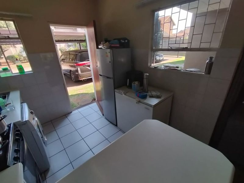 A functional kitchen featuring tiled flooring, tiled splashbacks, and built-in cabinetry, with direct access to the exterior driveway area.