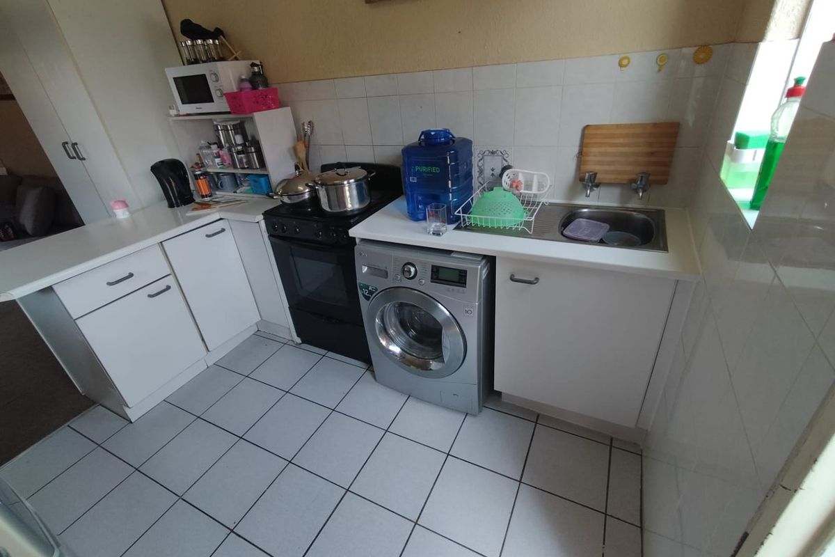 A functional kitchen featuring white cabinetry, tiled splashbacks, tiled flooring, a stainless steel sink, and space for a washing machine and freestanding stove.