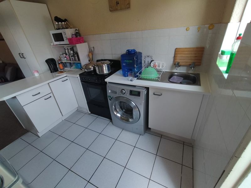 A functional kitchen featuring white cabinetry, tiled splashbacks, tiled flooring, a stainless steel sink, and space for a washing machine and freestanding stove.