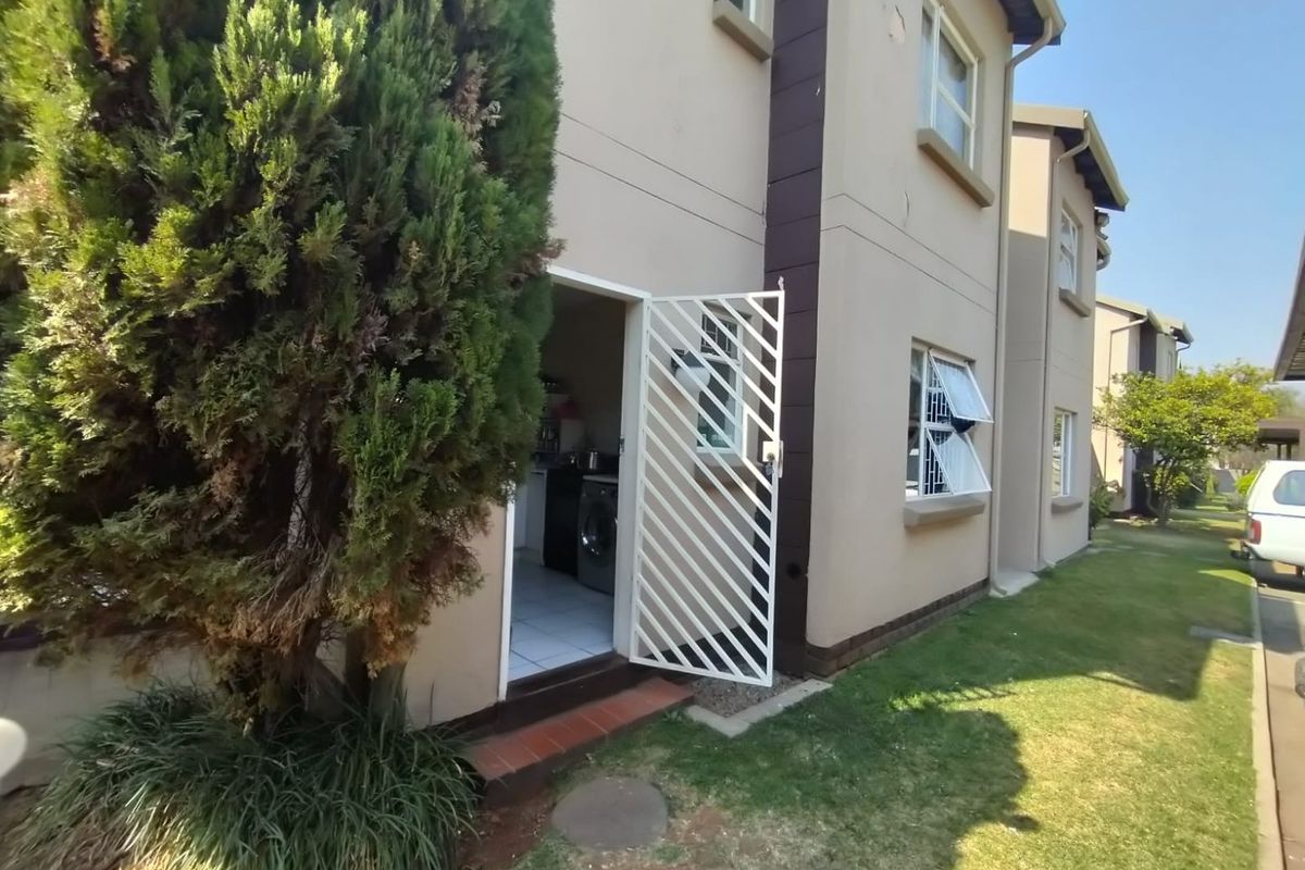 Rear exterior view of the townhouse featuring a security gate entrance, tiled threshold, and casement windows with security bars.