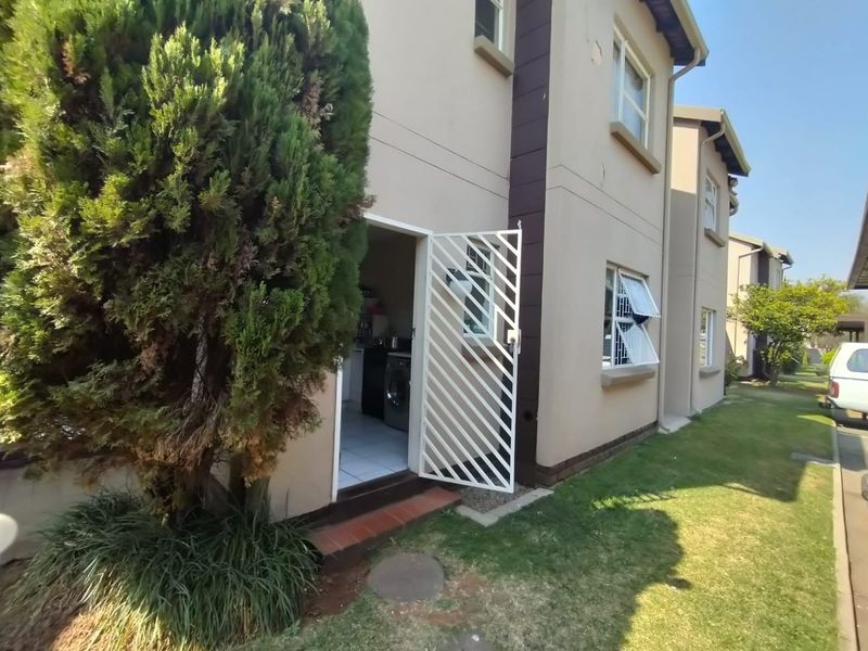 Rear exterior view of the townhouse featuring a security gate entrance, tiled threshold, and casement windows with security bars.