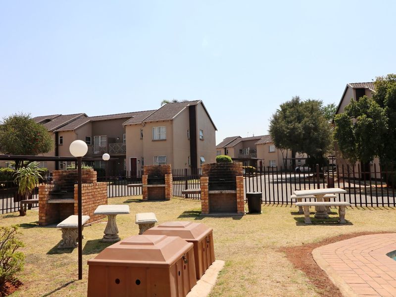 Communal outdoor area featuring multiple brick braai stands, paved pool surround, and metal perimeter fencing within a townhouse complex.