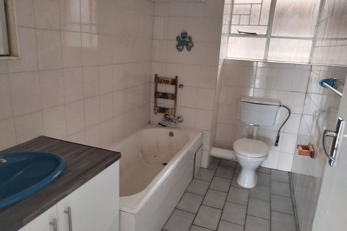A dated bathroom featuring a built-in vanity, bathtub, and toilet with tiled finishes throughout, offering potential for modernization and renovation.