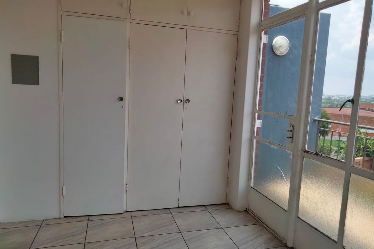 A bright, empty bedroom featuring built-in cupboards, tiled flooring, and a glass-paneled door leading to an outdoor area.