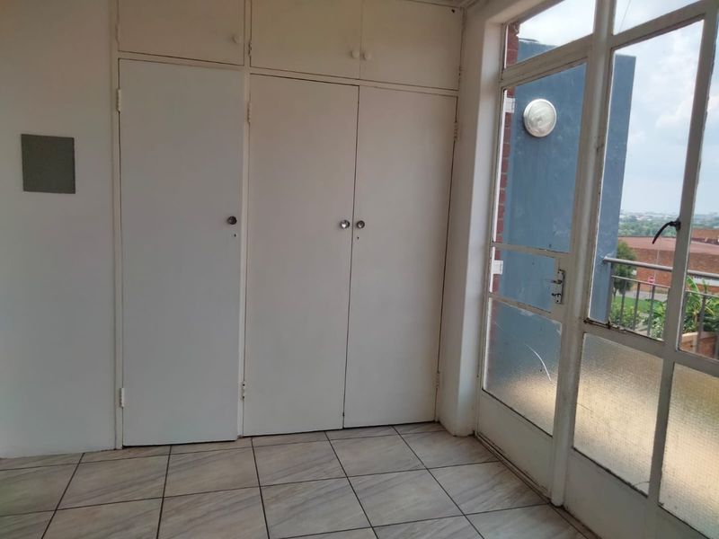 A bright, empty bedroom featuring built-in cupboards, tiled flooring, and a glass-paneled door leading to an outdoor area.