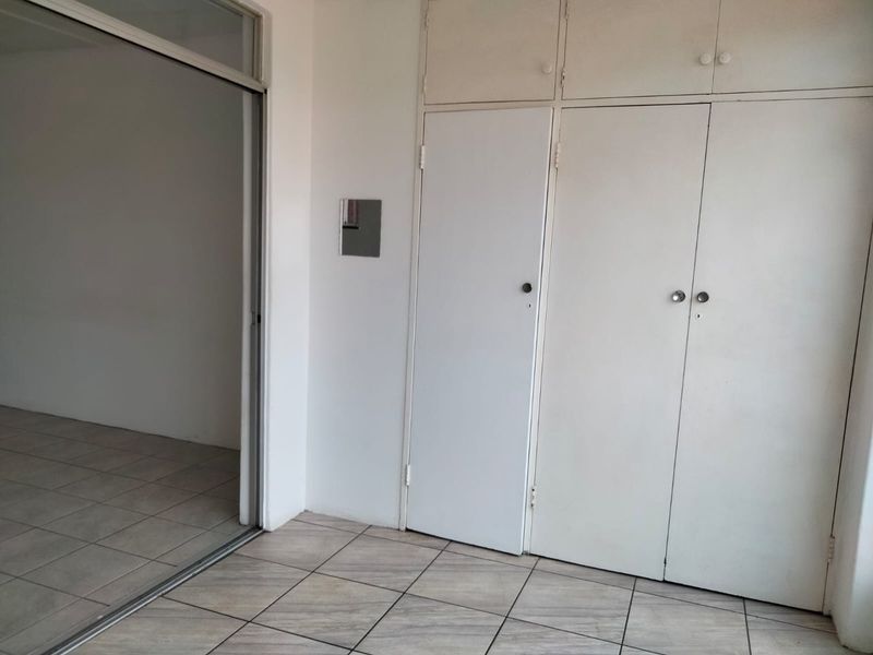 An empty bedroom featuring tiled flooring and ample built-in cupboard storage with a sliding door leading to an adjacent space.