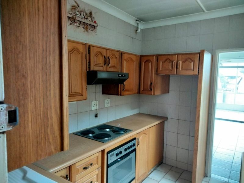 A dated kitchen featuring wooden cabinetry, laminate countertops, and built-in cooking appliances with tiled splashbacks and flooring.