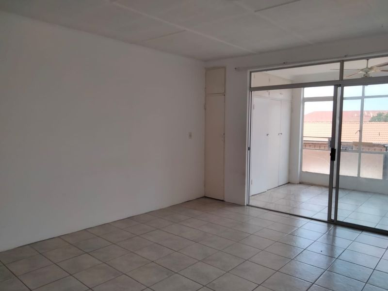 An empty living room featuring tiled flooring, built-in storage cupboards, and a sliding glass door leading to an enclosed balcony area.
