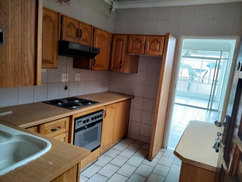 A dated kitchen featuring wooden cabinetry, laminate countertops, built-in oven, and hob, with tiled flooring and direct access to an adjacent patio area.