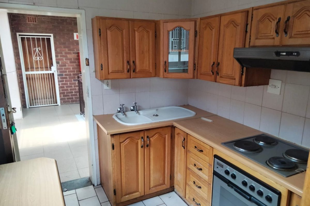 A functional kitchen featuring wooden cabinetry, laminate countertops, a built-in oven with electric hob, and tiled splashbacks, providing a practical workspace.