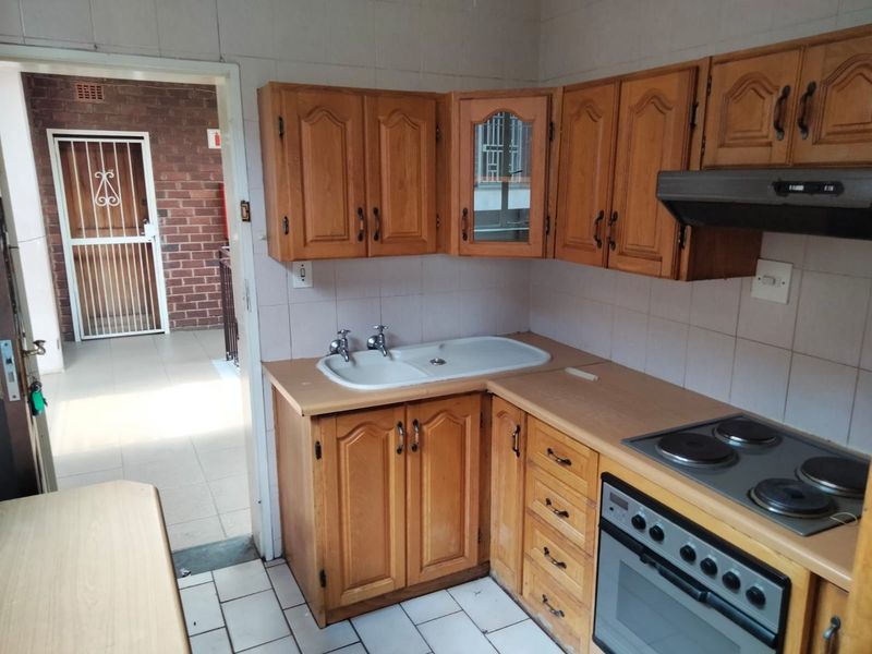 A functional kitchen featuring wooden cabinetry, laminate countertops, a built-in oven with electric hob, and tiled splashbacks, providing a practical workspace.