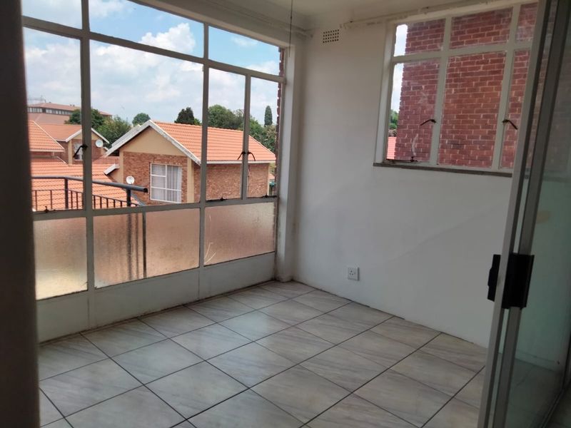 An enclosed balcony or sunroom featuring tiled flooring and large windows, offering a bright, versatile space with views of the surrounding townhouse complex.
