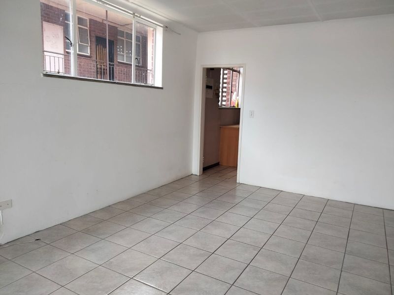 An empty, neutrally painted living area featuring tiled flooring and a large window, providing a blank canvas for interior design.