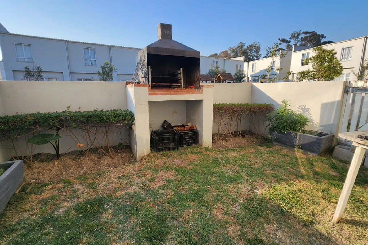 Rear garden area featuring a built-in masonry braai, boundary walls, and established garden beds in a townhouse setting.