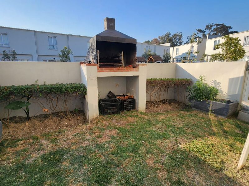 Rear garden area featuring a built-in masonry braai, boundary walls, and established garden beds in a townhouse setting.