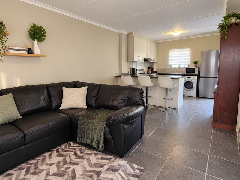 An open-plan living and kitchen area featuring tiled flooring, a functional kitchen island with breakfast bar seating, and an adjacent staircase.