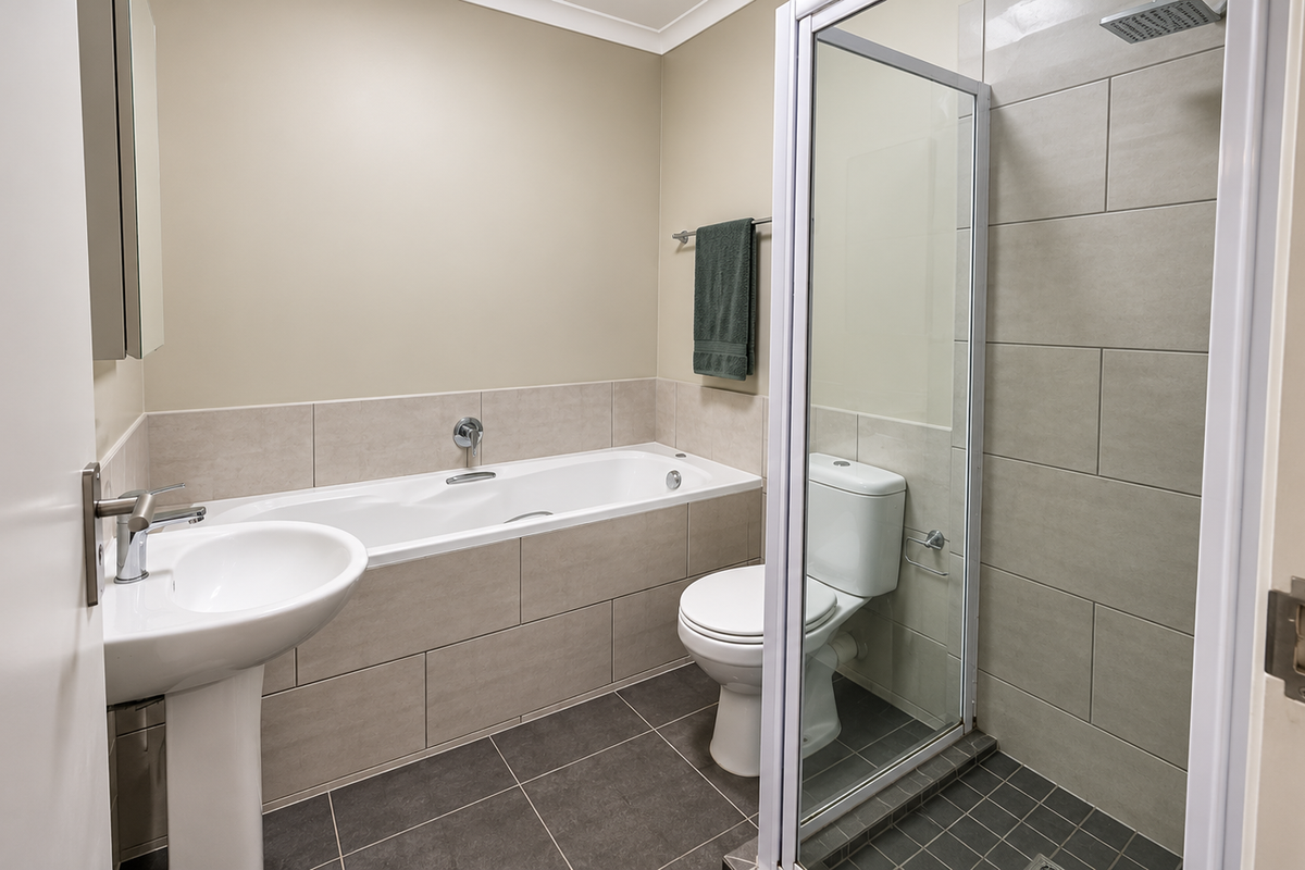 A clean, modern bathroom featuring a pedestal basin, a built-in bathtub, a separate glass-enclosed shower, and neutral wall and floor tiling.