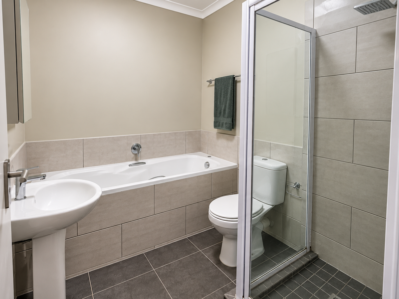 A clean, modern bathroom featuring a pedestal basin, a built-in bathtub, a separate glass-enclosed shower, and neutral wall and floor tiling.