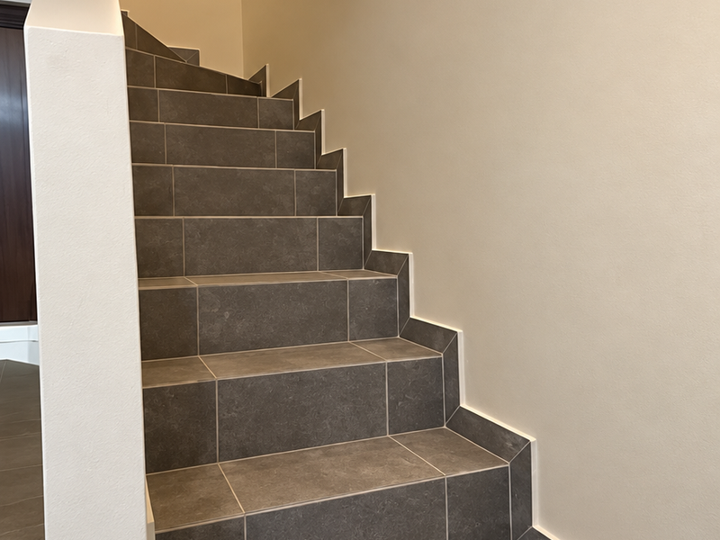 A clean, modern staircase featuring dark grey ceramic floor tiles and neutral painted walls, providing a sleek transition between levels.