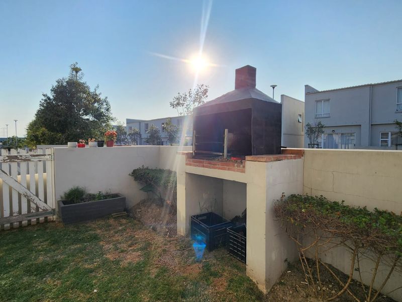 Rear garden area featuring a built-in braai, perimeter boundary wall, and a timber access gate.