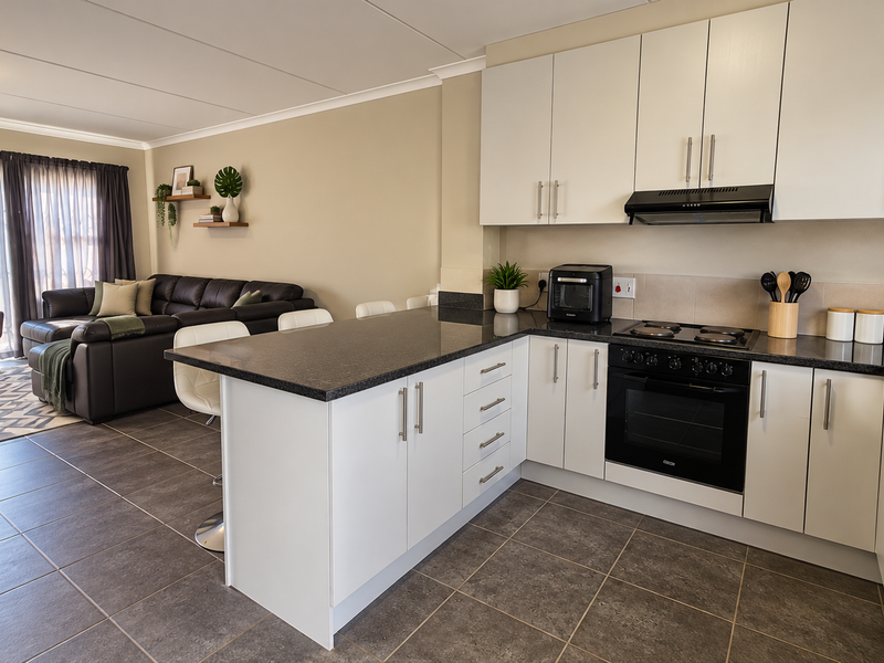 Modern open-plan kitchen and living area featuring sleek white cabinetry, granite countertops, built-in appliances, and tiled flooring leading to a bright lounge space.